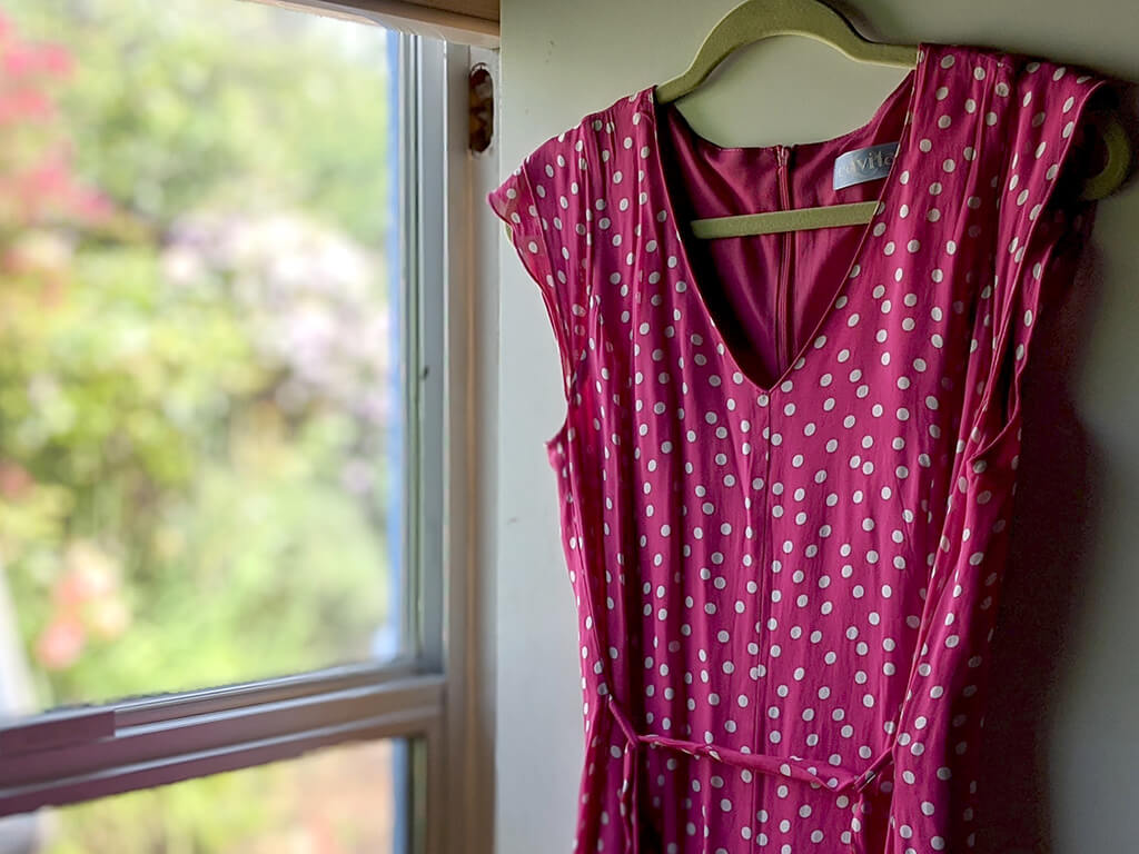 Pink polkadot chiffon summer dress hanging on a close hanger by a window.