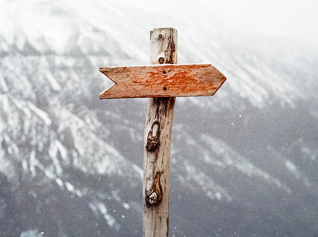 A wooden arrow pointing to the right, backed by snowy mountains